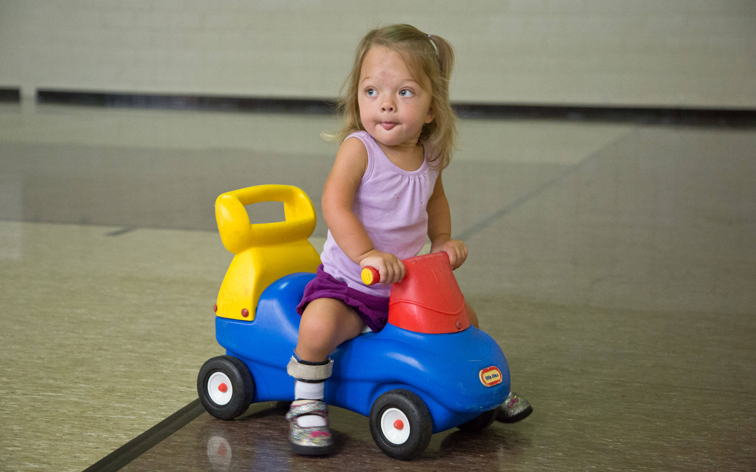 Evie, diagnosed with HPP at 2 weeks old, riding a toy car